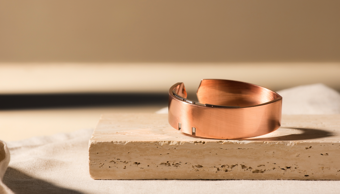 Copper-toned magnetic cuff bracelet on warm ivory stone and linen